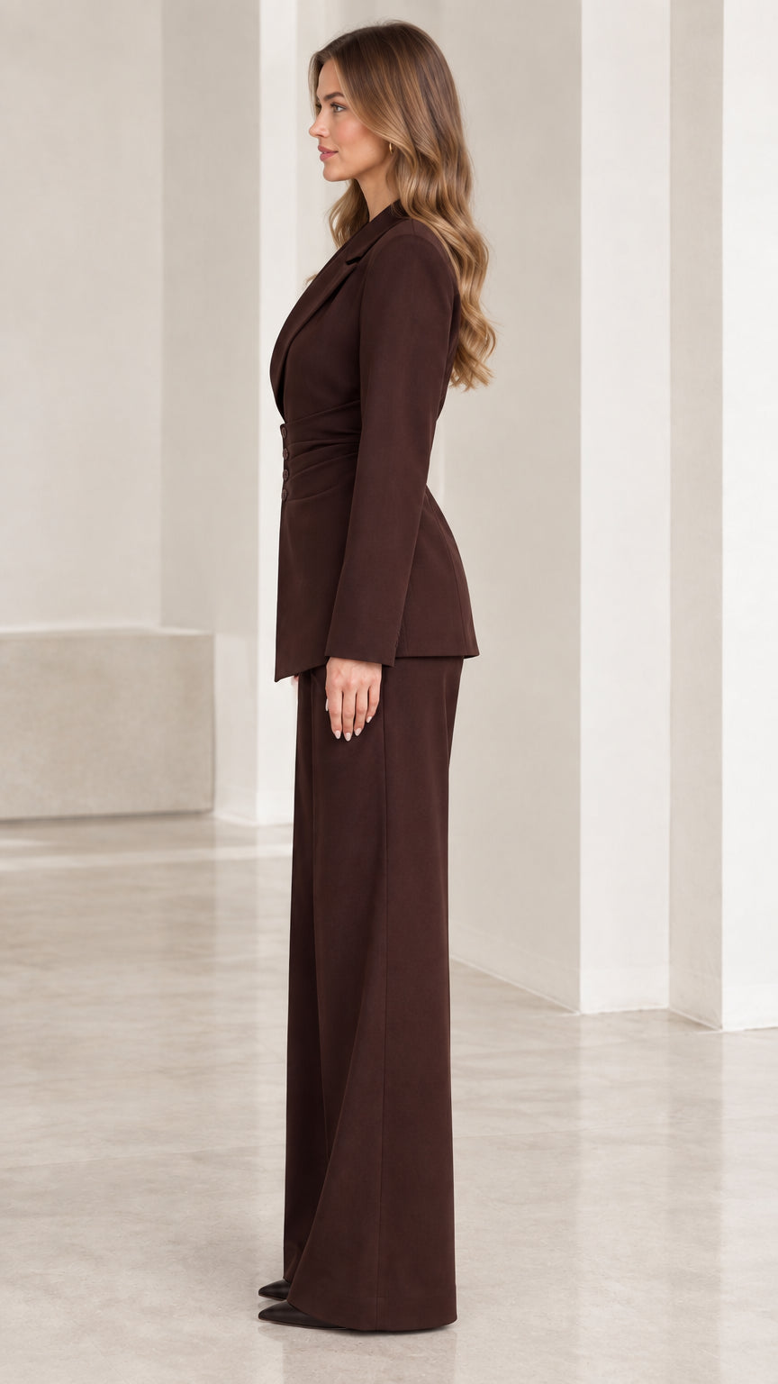 Side profile view of woman modeling chocolate brown tailored two-piece pantsuit